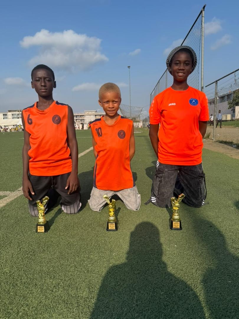 Trois trophées dorés UCFFY posés sur le terrain devant trois jeunes joueurs