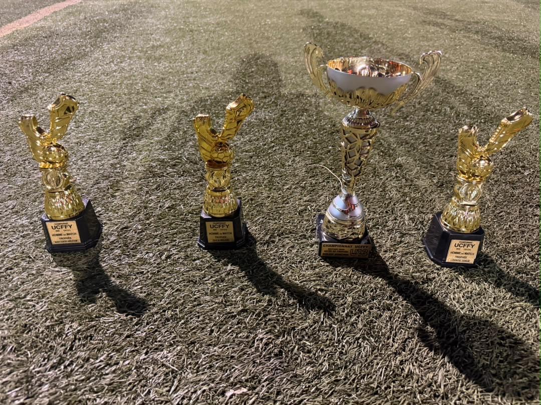 Gros plan sur les trophées du Championnat UCFFY posés sur la pelouse