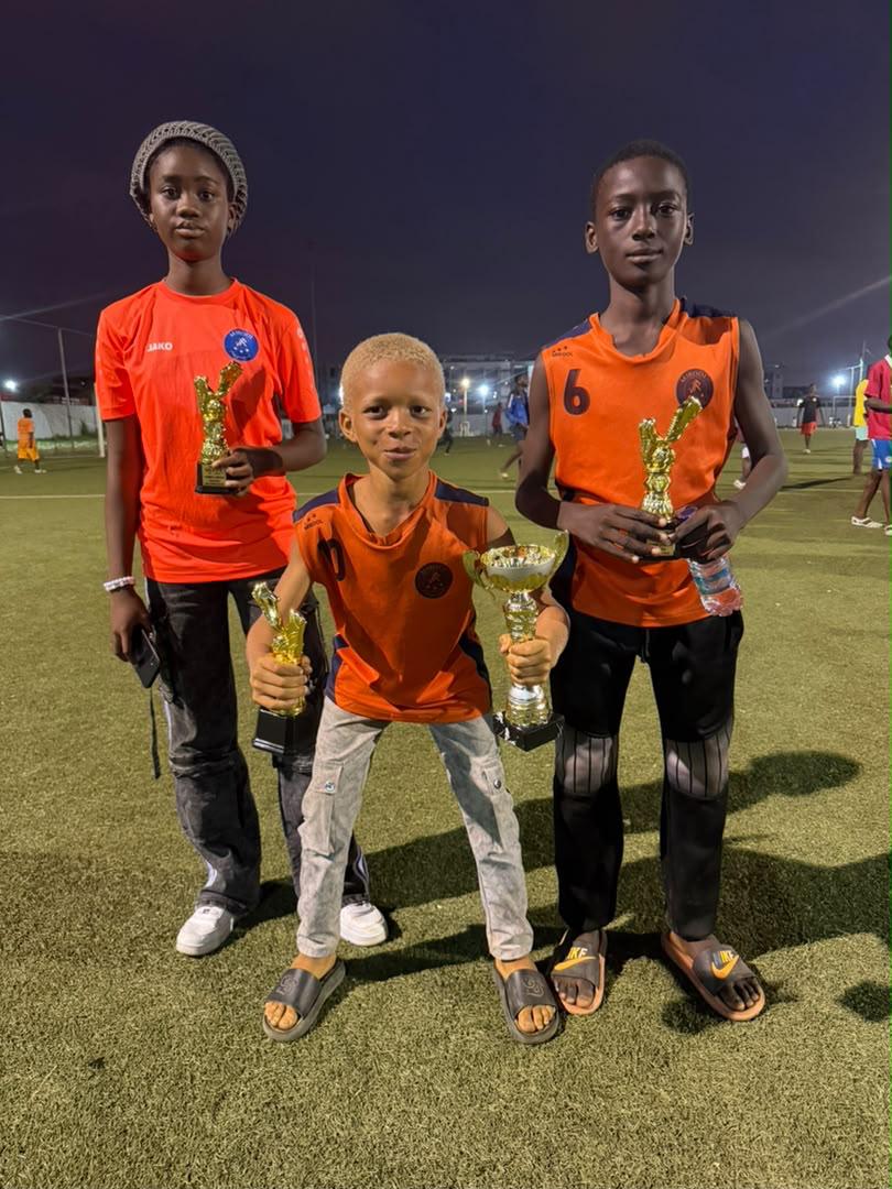 Trois jeunes joueurs de JR MIROOL CI tenant leurs trophées sur un terrain de Yopougon